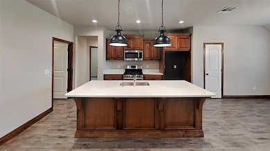 Kitchen featuring appliances with stainless steel finishes, light countertops, recessed lighting, a center island with sink, and hanging light fixtures
