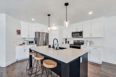 Kitchen featuring a center island with sink, white cabinets, appliances with stainless steel finishes, pendant lighting, and a breakfast bar