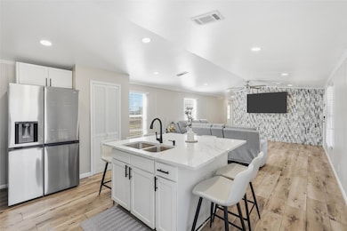 Kitchen with a kitchen bar, stainless steel fridge, white cabinets, light wood-style floors, and recessed lighting