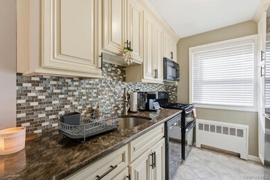 Kitchen with decorative backsplash, cream cabinets, radiator heating unit, dark stone counters, and black appliances
