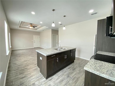 Kitchen featuring baseboards, a sink, light wood-style floors, a raised ceiling, and a center island with sink