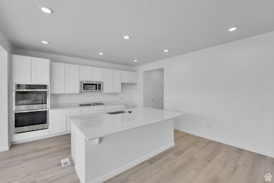 Kitchen with white cabinets, an island with sink, light stone countertops, light wood-style floors, and recessed lighting