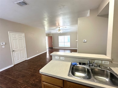 Kitchen featuring light countertops, open floor plan, dark wood-type flooring, brown cabinets, and ceiling fan