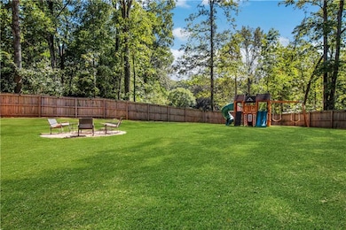 Fenced backyard featuring a patio, a playground, an outdoor fire pit, and view of wooded area