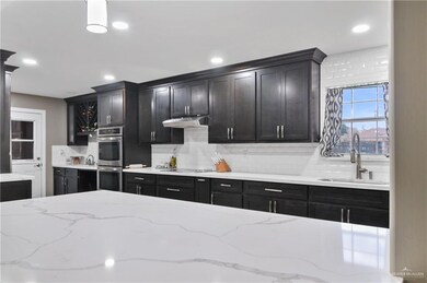 Kitchen with double oven, sink, light stone countertops, and backsplash