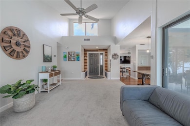 This spacious living room features dramatic vaulted ceilings creates an impressive sense of height and openness. The room is enhanced by abundant natural light streaming through a large upper window, while a ceiling fan provides comfortable air circulation.The neutral carpet flooring flows seamlessly throughout the space, connecting this living area to the adjacent kitchen and dining spaces in a true open-concept design. The layout offers excellent sightlines across the main living areas, creating a cohesive and welcoming environment.