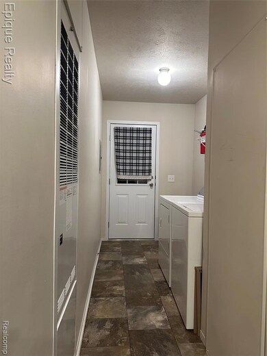 Washroom featuring a textured ceiling, independent washer and dryer, a heating unit, and stone finish flooring