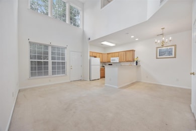 Unfurnished living room featuring a chandelier, light carpet, a high ceiling, and recessed lighting