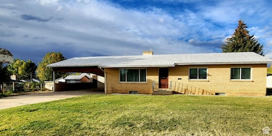 Ranch-style home featuring brick siding, driveway, a front yard, a chimney, and a carport