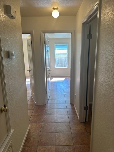 Hall featuring a textured wall, tile patterned floors, and a textured ceiling