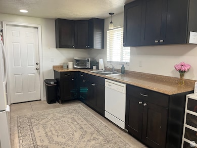 Kitchen with white appliances, dark cabinetry, a textured ceiling, light tile patterned flooring, and recessed lighting