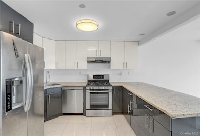 Kitchen with stainless steel appliances, light stone countertops, light marble finish flooring, and white cabinetry