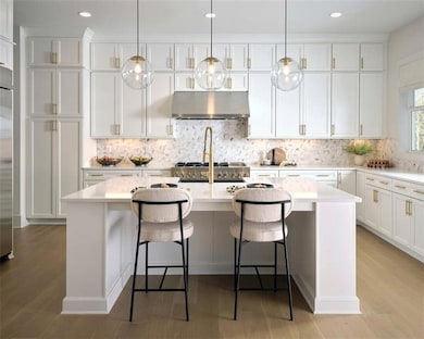 Photo from the Roswell Model Home: Kitchen with under cabinet range hood, backsplash, an island with sink, white cabinets, and recessed lighting