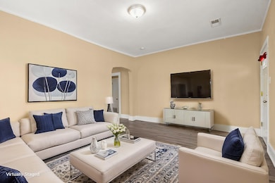 Living room with baseboards, crown molding, visible vents, arched walkways, and wood finished floors