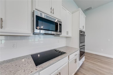Kitchen with stainless steel appliances, white cabinetry, light stone counters, and decorative backsplash