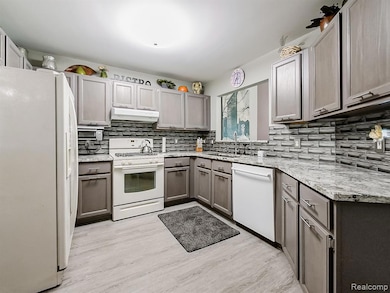 Kitchen featuring white appliances, light wood finished floors, decorative backsplash, light stone counters, and under cabinet range hood