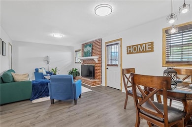 Living area featuring healthy amount of natural light, wood finished floors, a brick fireplace, and ornamental molding