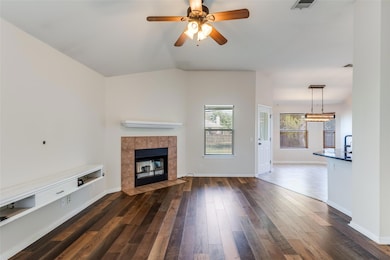 Unfurnished living room featuring dark wood-type flooring, a tile fireplace, ceiling fan, and lofted ceiling