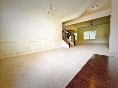Unfurnished living room with a decorative wall, carpet floors, a wainscoted wall, stairway, and a chandelier