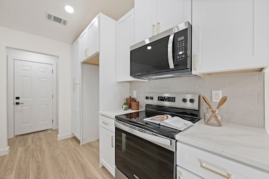 Kitchen featuring stainless steel appliances, white cabinetry, backsplash, light wood-type flooring, and recessed lighting