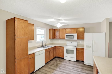 kitchen featuring white appliances, light wood finished floors, light countertops, brown cabinets, and a textured ceiling