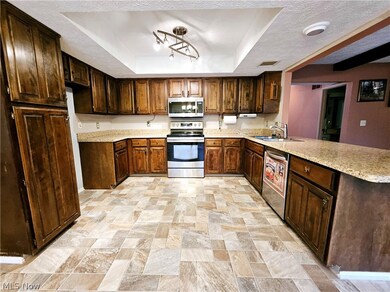 Kitchen featuring sink, light stone-look counters, tray ceiling, appliances with stainless steel finishes