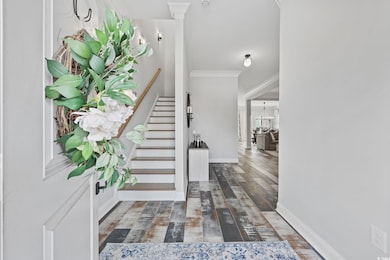 Foyer entrance with ornamental molding, stairway, a chandelier, and wood finished floors