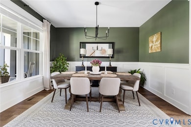 Dining area featuring dark wood-style floors, a decorative wall, wainscoting, and a chandelier
