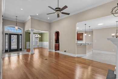 Entryway with crown molding, light wood-style floors, ceiling fan with notable chandelier, arched walkways, and ornate columns