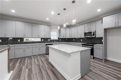 Kitchen with gray cabinets, stainless steel appliances, a kitchen island, hanging light fixtures, and recessed lighting