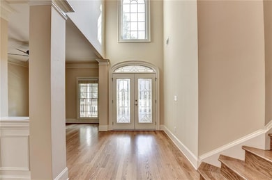 Entryway featuring a towering ceiling, light wood-type flooring, french doors, crown molding, and stairs