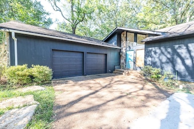 View of side of home with concrete driveway, stone siding, a garage, and roof with shingles