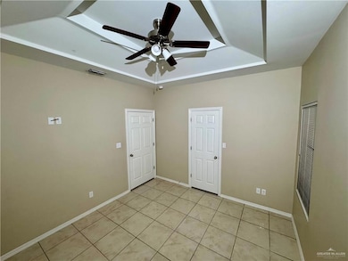 Spare room with light tile patterned floors, baseboards, visible vents, ceiling fan, and a tray ceiling