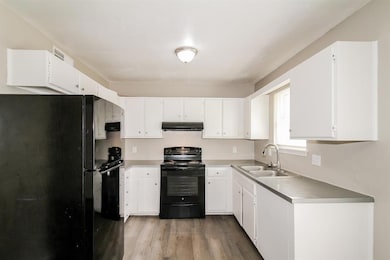 Kitchen with black appliances, light wood-type flooring, white cabinetry, under cabinet range hood, and light countertops