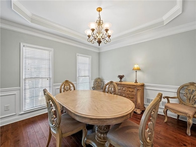 Dining space featuring a wainscoted wall, a decorative wall, a chandelier, crown molding, and a raised ceiling