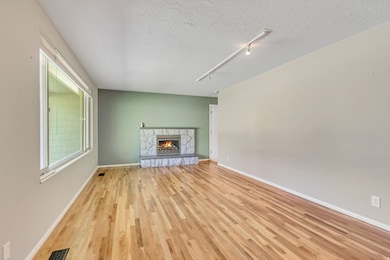 Unfurnished living room featuring rail lighting, a stone fireplace, light wood-style flooring, and a textured ceiling