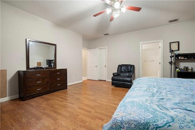 Bedroom with light wood-style floors, a textured ceiling, ceiling fan, and connected bathroom