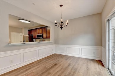 Unfurnished dining area with a wainscoted wall, light wood-style floors, a decorative wall, and a chandelier