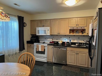 Kitchen featuring stainless steel appliances, dark countertops, decorative backsplash, and light brown cabinets