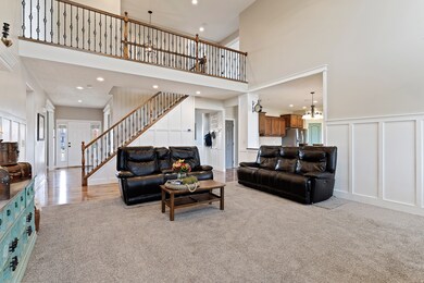 Living area featuring a chandelier, a towering ceiling, light colored carpet, a decorative wall, and recessed lighting