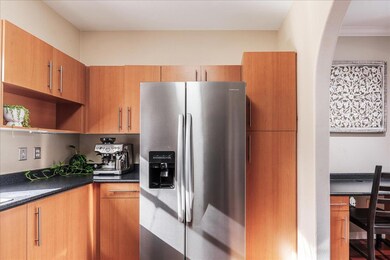 Kitchen with stainless steel refrigerator with ice dispenser, open shelves, an office area, brown cabinets, and dark stone counters
