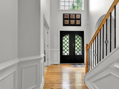 Foyer entrance with a decorative wall, light wood-style floors, a high ceiling, wainscoting, and stairway