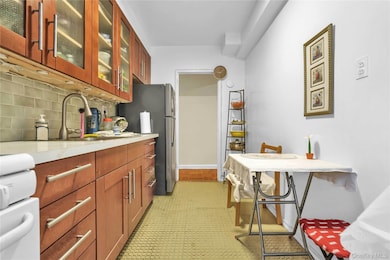 Kitchen with freestanding refrigerator, backsplash, glass insert cabinets, light floors, and a sink