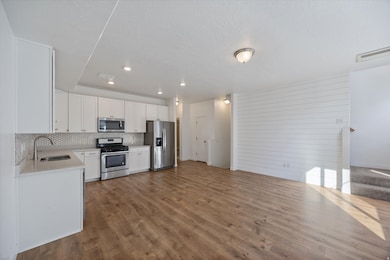 Kitchen featuring white cabinetry, stainless steel appliances, dark wood-style flooring, decorative backsplash, and light stone countertops