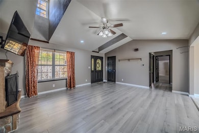 Unfurnished living room featuring lofted ceiling, light wood-type flooring, a fireplace with raised hearth, and ceiling fan