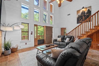 Tiled living room featuring a towering ceiling, a ceiling fan, and stairs