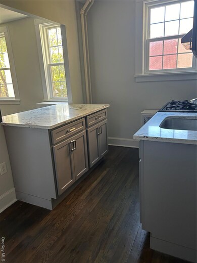 Kitchen with healthy amount of natural light, light stone countertops, gray cabinetry, and dark wood-style floors