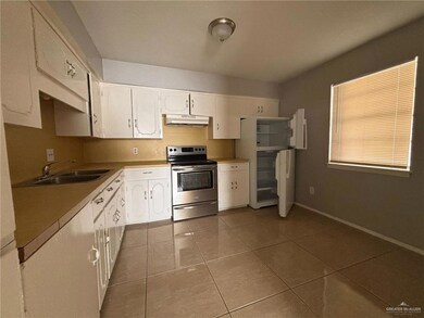 Kitchen with appliances with stainless steel finishes, range hood, light tile patterned floors, white cabinets, and light countertops