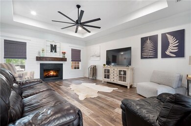 Living area featuring a raised ceiling, a ceiling fan, wood finished floors, a warm lit fireplace, and ornamental molding