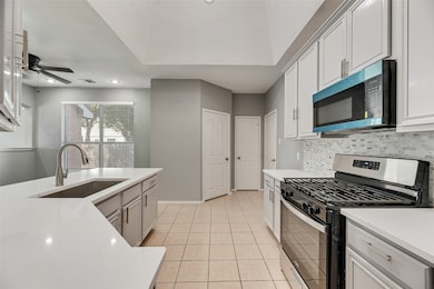 Kitchen featuring appliances with stainless steel finishes, light tile patterned floors, white cabinetry, backsplash, and light stone countertops